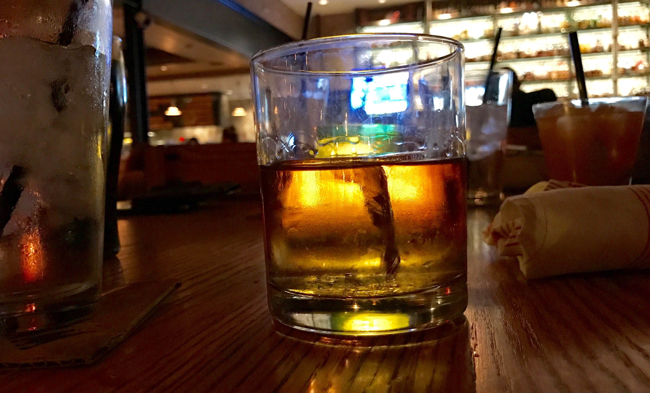 A glass of whiskey on a table backlit by a bar prior to a DWI