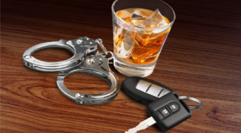 A wooden countertop with a glass of whiskey, handcuffs, and car keys.