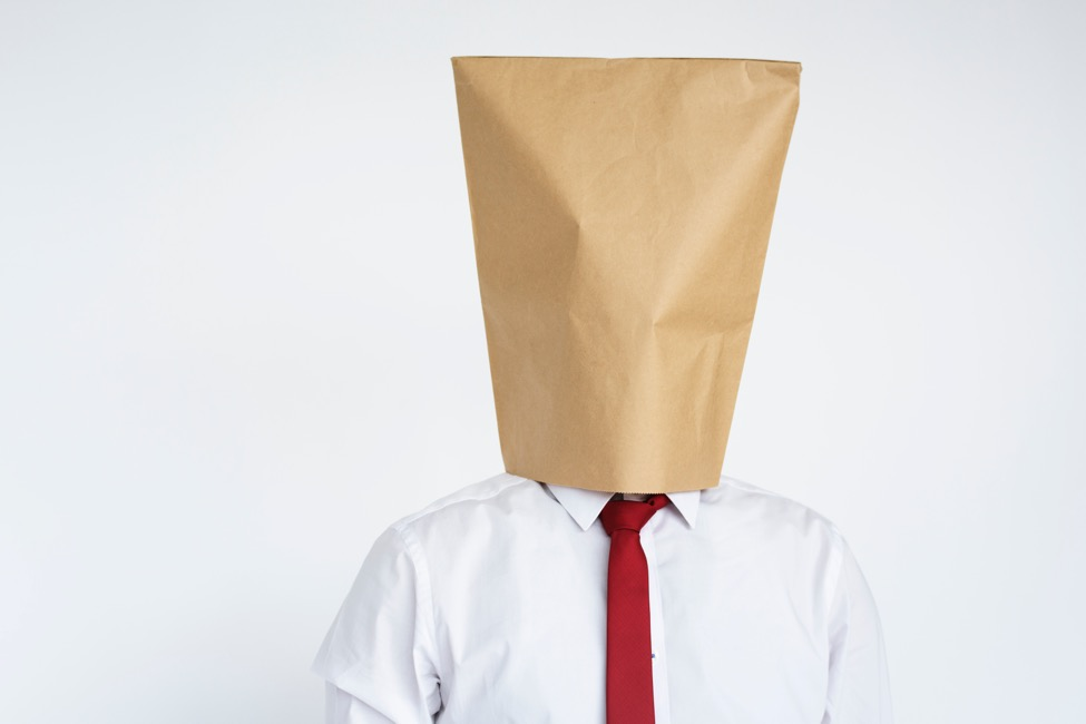 A man in white shirt stands with a paper bag over his head